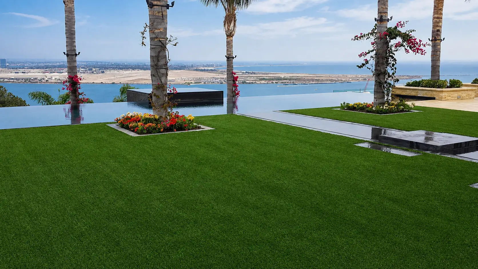 Artificial turf lawn with palm trees, planted beds, and a coastal view